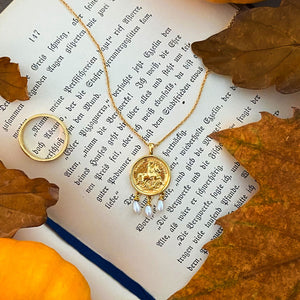 Gold engraved horse coin necklace with hanging pearls, surrounded by autumn leaves and pumpkins