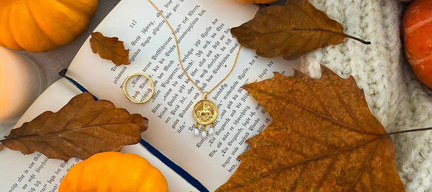 Gold engraved horse coin necklace with hanging pearls, surrounded by autumn leaves and pumpkins