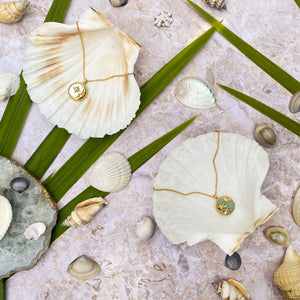 Semi precious sun and moon coin necklaces on shells surrounded by palm leaves