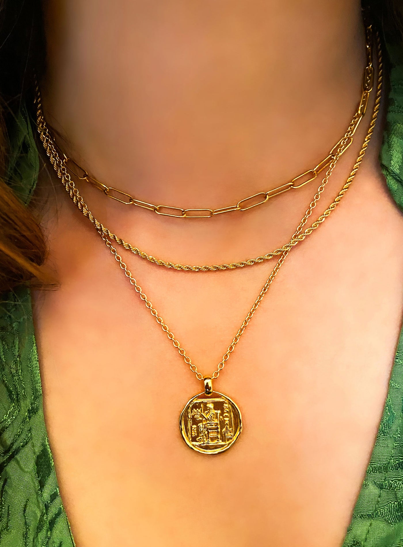 Model wearing gold twist rope necklace, chunky chain and gold engraved greek coin pendant