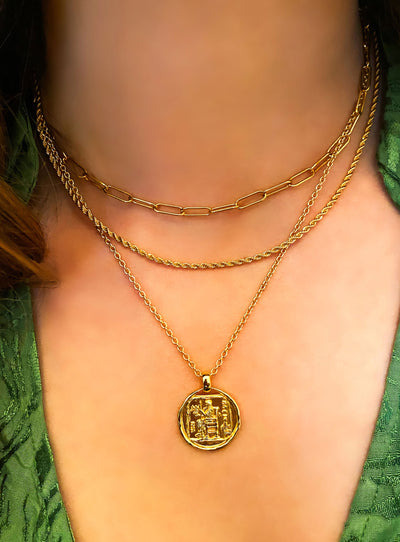 Model wearing gold twist rope necklace, chunky chain and gold engraved greek coin pendant