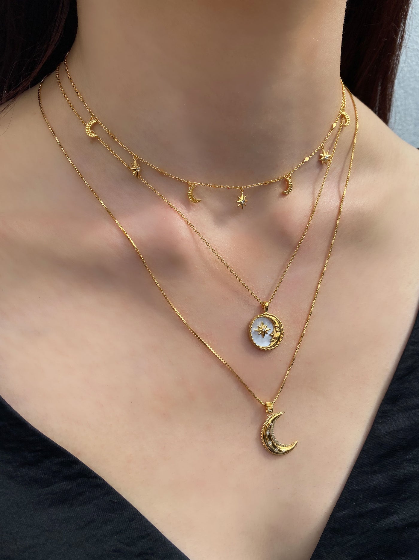 Model wearing gold moon and star choker with CZ crystals, layered with engraved mother of pearl moon, coin pendant and moon necklace 