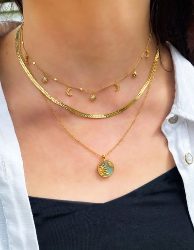 Model wearing gold moon and star choker with CZ crystals layered with snake chain necklace and engraved amazonite sun pendant