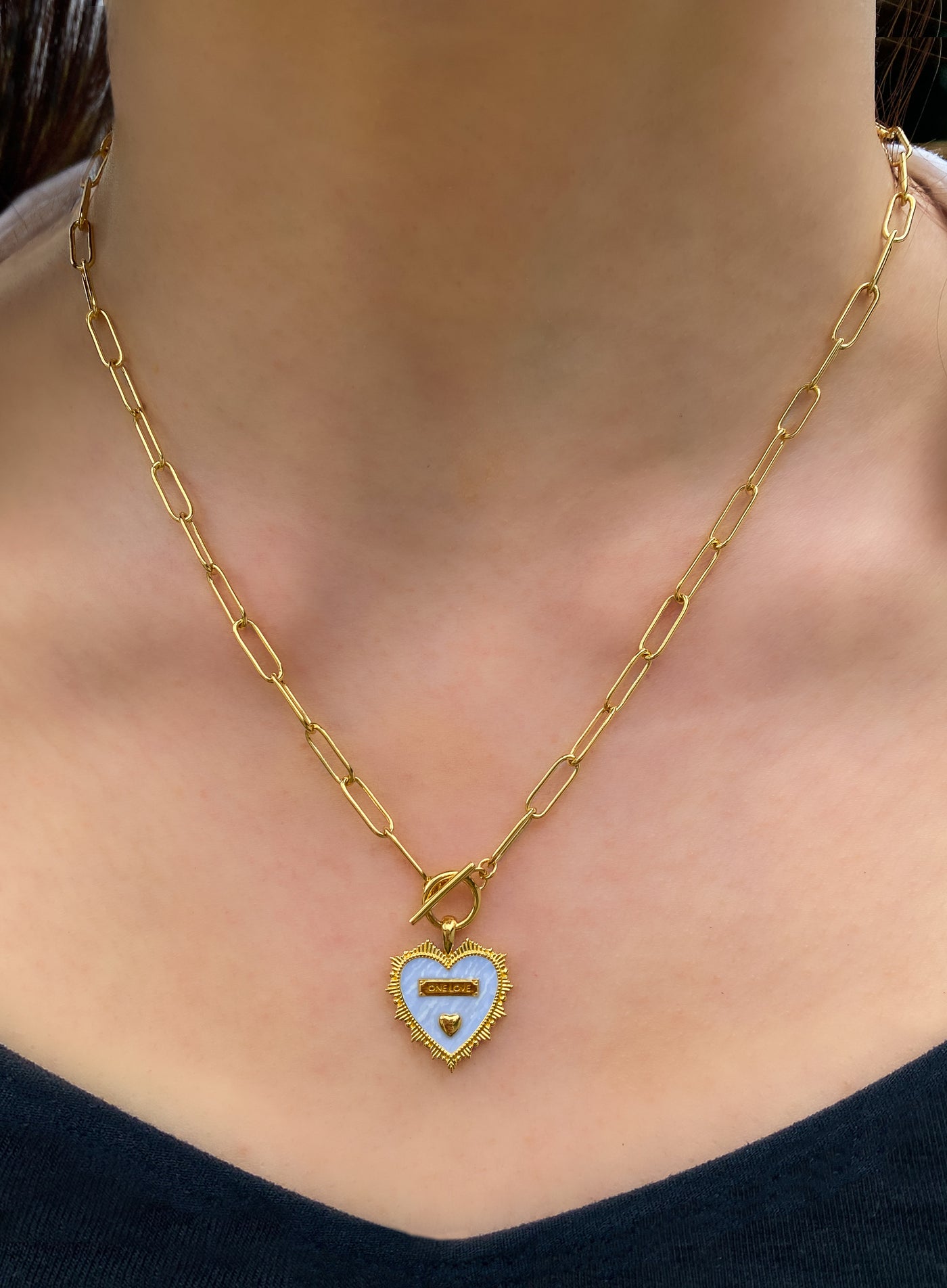 Model wearing gold plated brass heart pendant on chunky chain with light blue enamel base, engraved wording and engraved edging