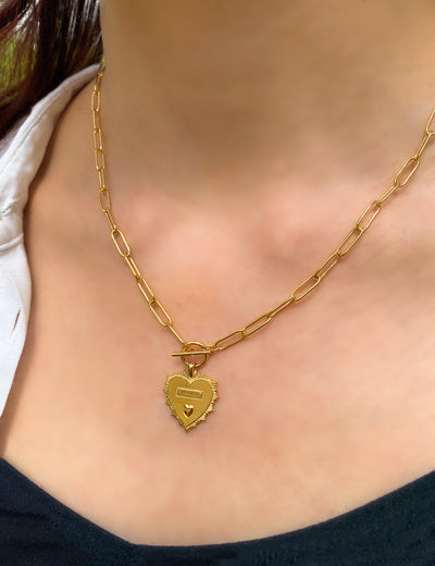 Model wearing gold plated brass heart pendant on chunky chain with engraved Greek wording and engraved edging